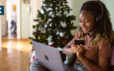 Online Shopperin sitzt mit dem Laptop auf dem Sofa. Im Hintergrund ist ein geschmückter Weihnachtsbaum.